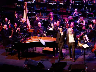 Two men standing in front of a piano and string orchestra.