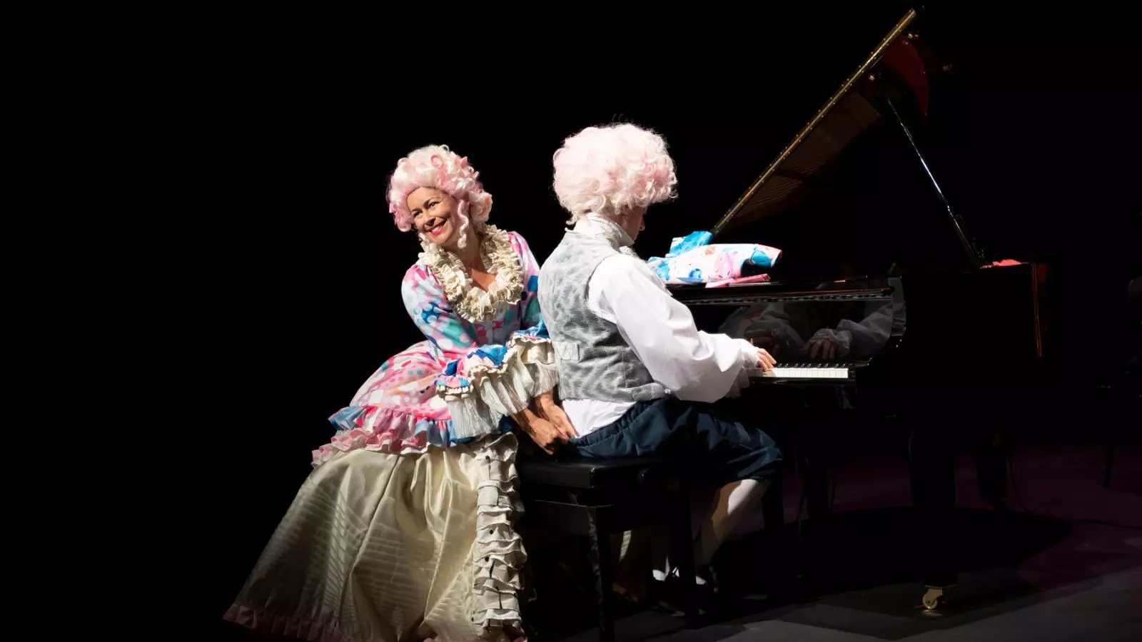 A man and woman dressed up as Mozart and his wife in colourful outfits and big white wigs