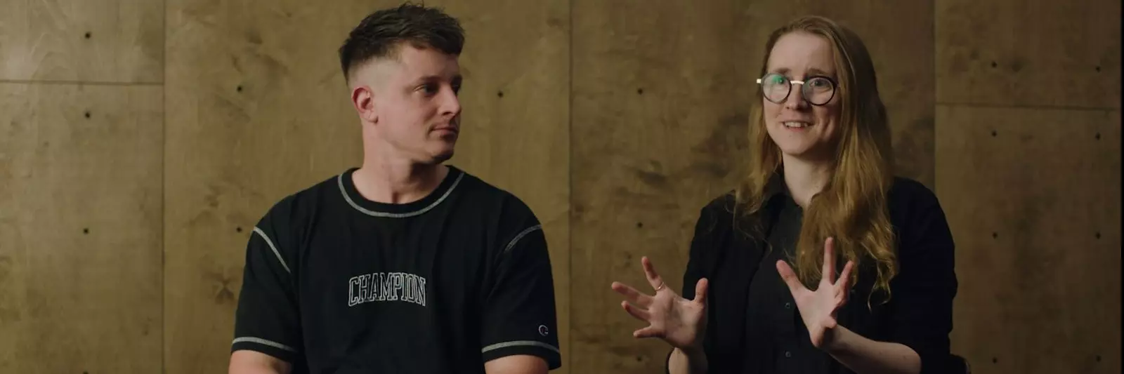 A white man with a short haircut looks at a woman to our right. She is white with long blonde hair, round clear glasses and had her hands in front of her as if mid-discussion.