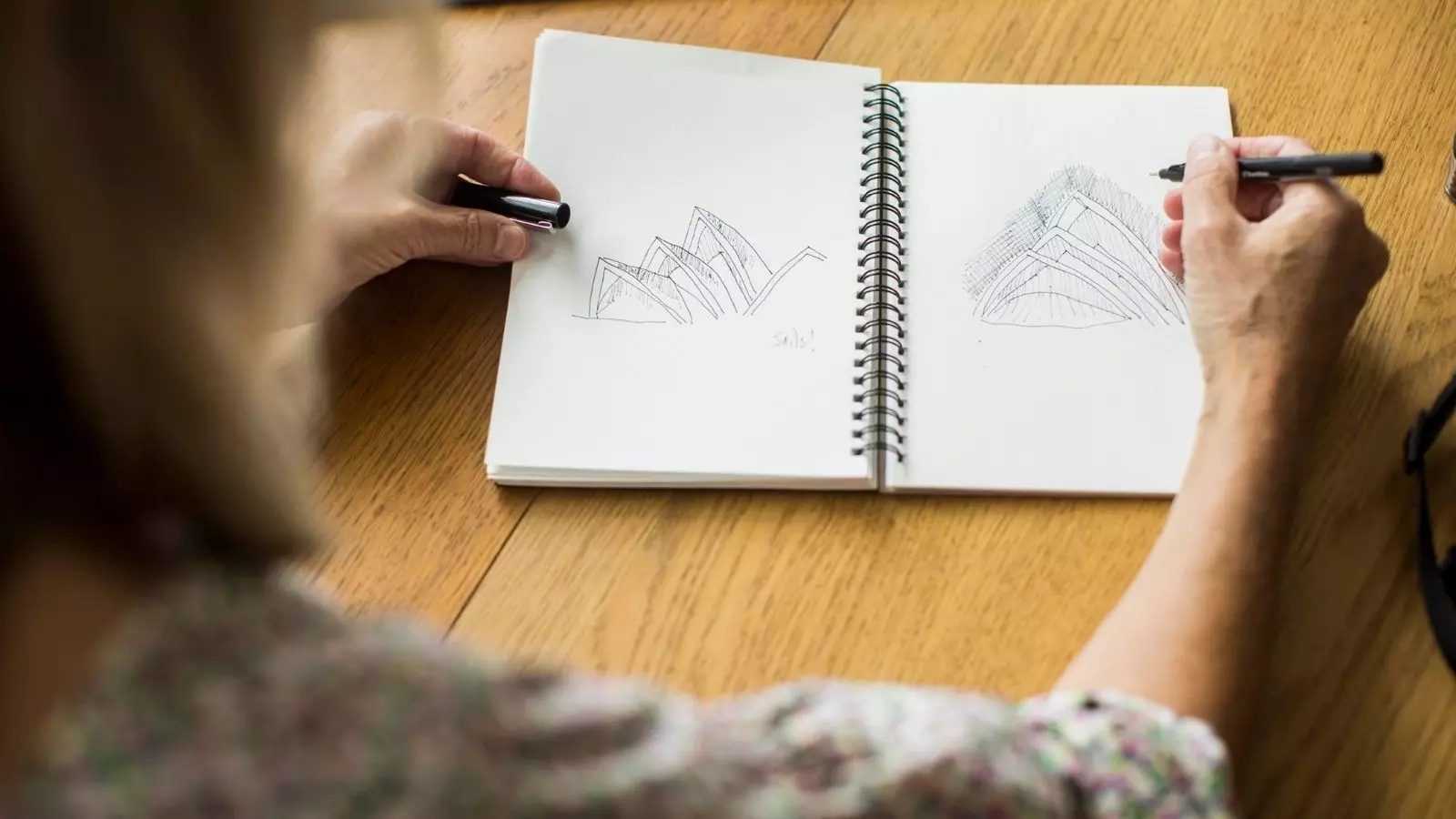 A woman drawing sketches of the Sydney Opera House in a notebook.