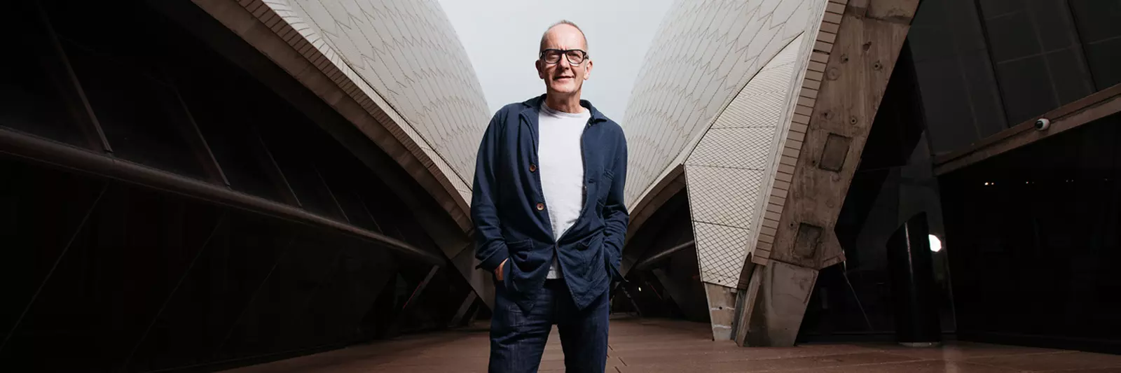 A man in glasses and a suit standing outside the Sydney Opera House.