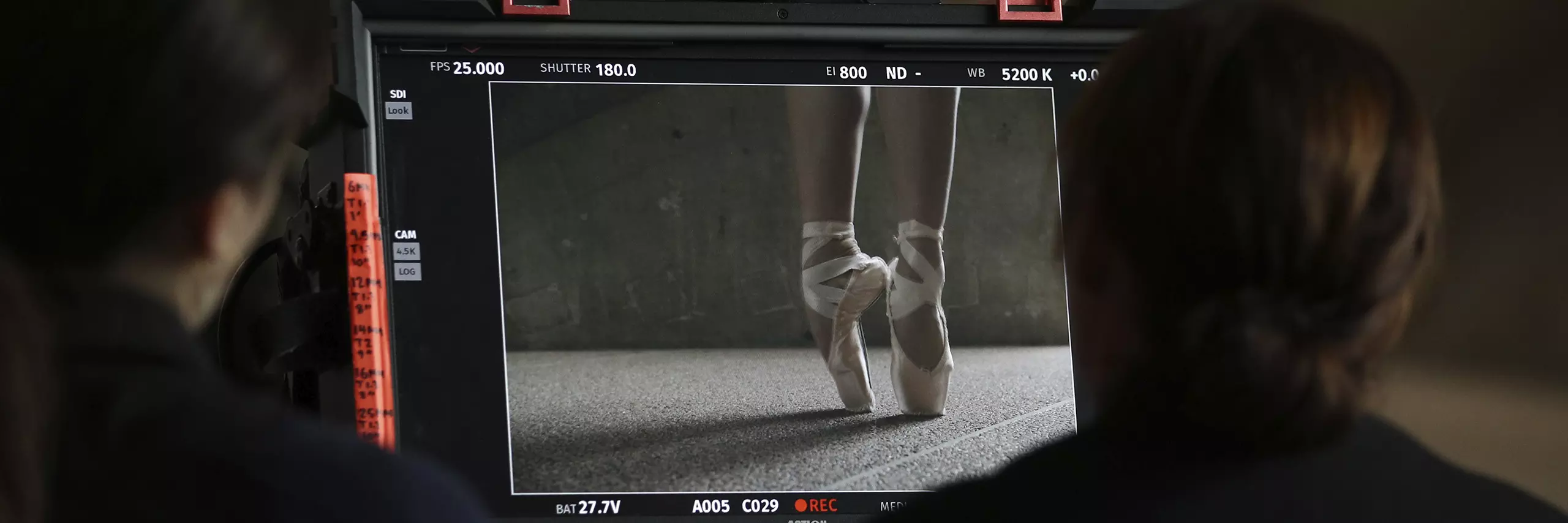 Two people looking at a video screen, showing an image of a ballerina's shoes and feet, on pointe.