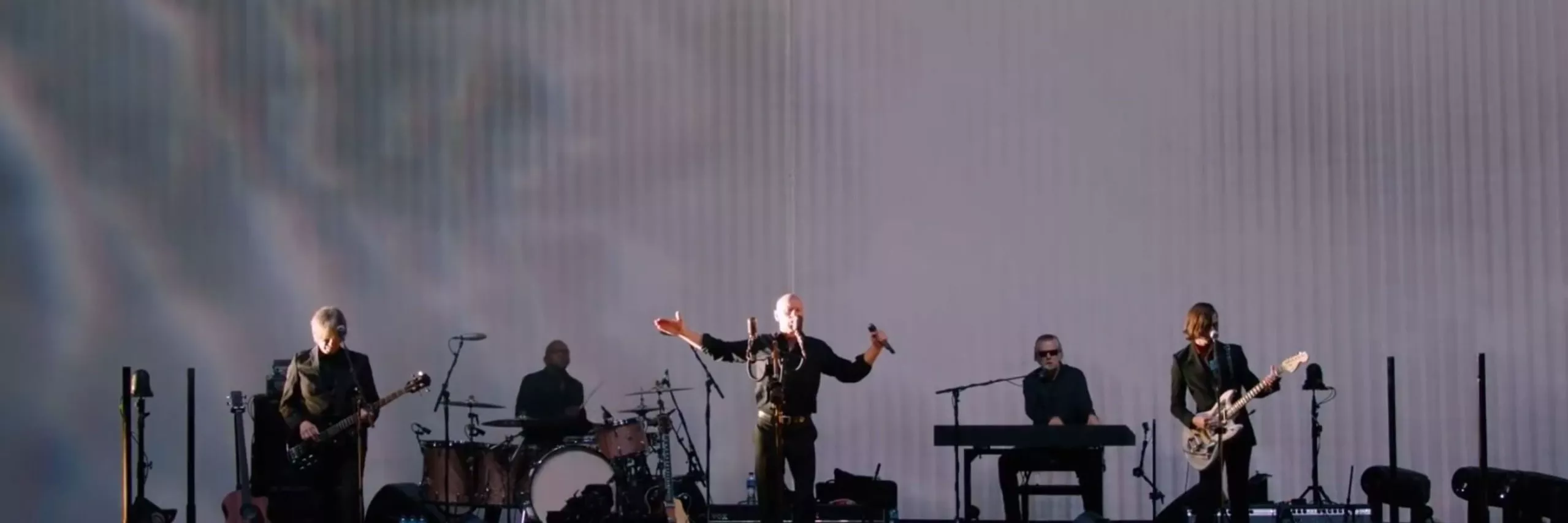 A group of individuals on stage, with a man at the forefront passionately singing into a microphone.