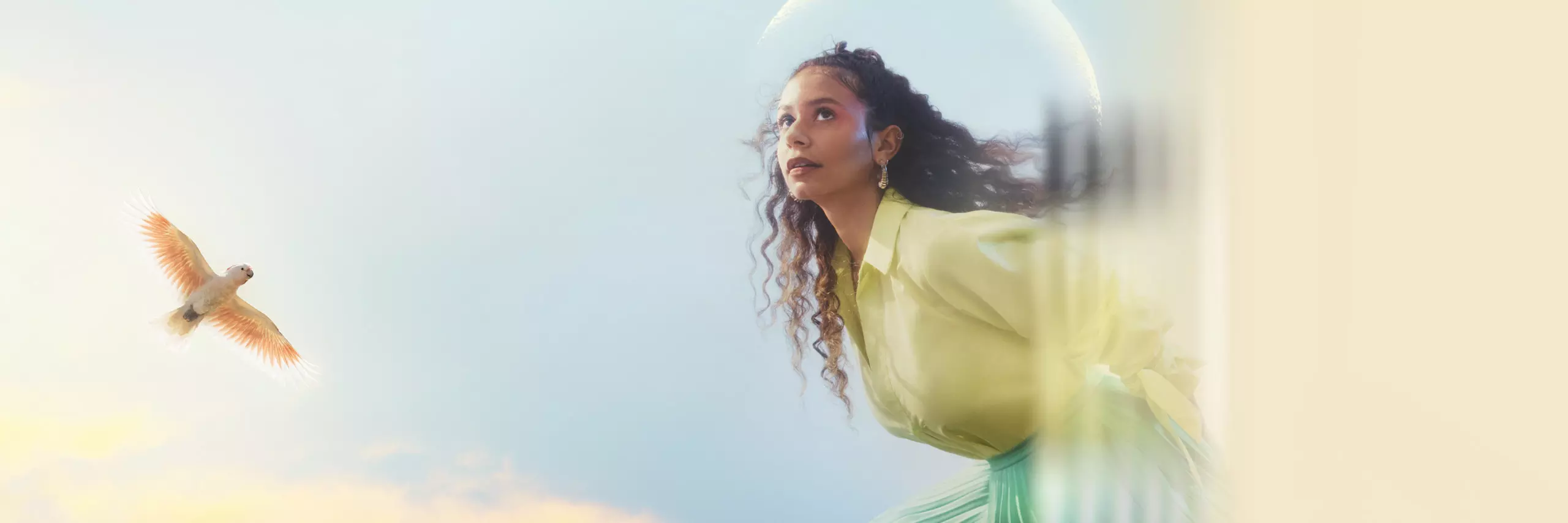 A performer wears a light green blouse with pink eyeshadow looks off camera, the moon and a bird is seen behind her