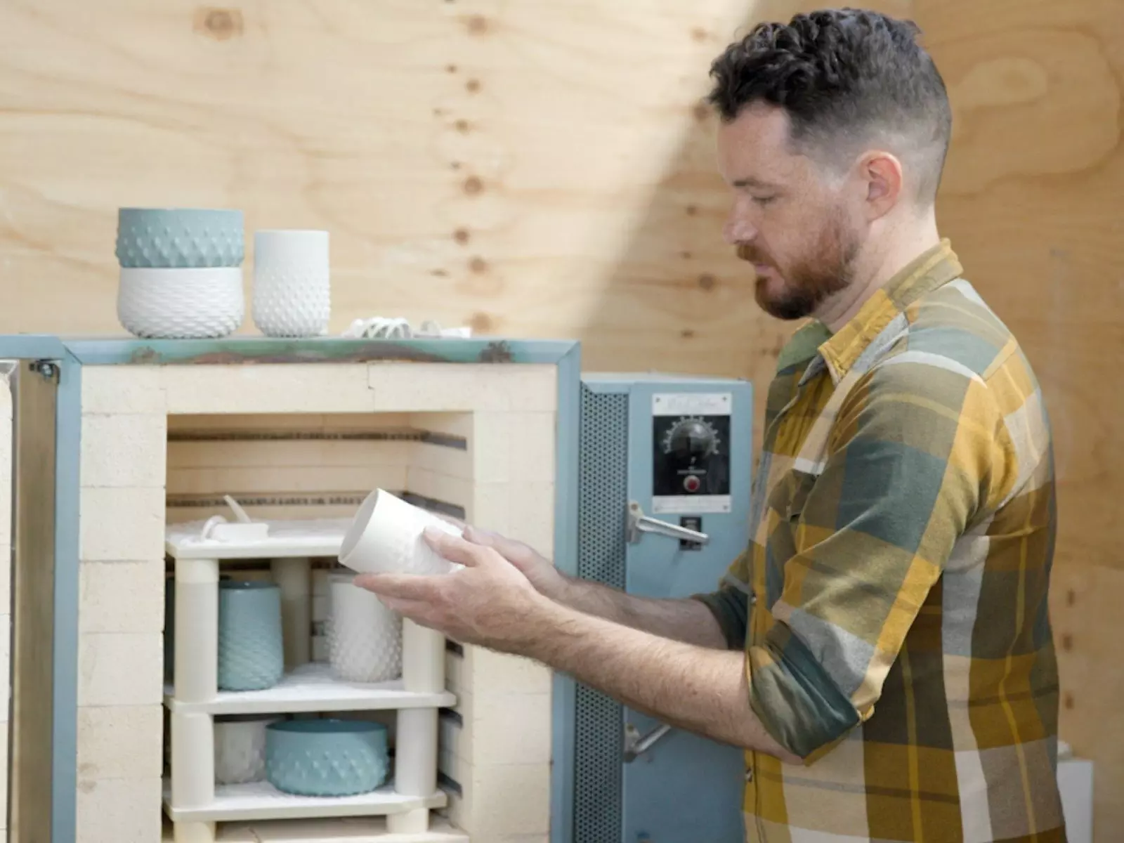 A man in a shirt crafting a white object in a wooden room.